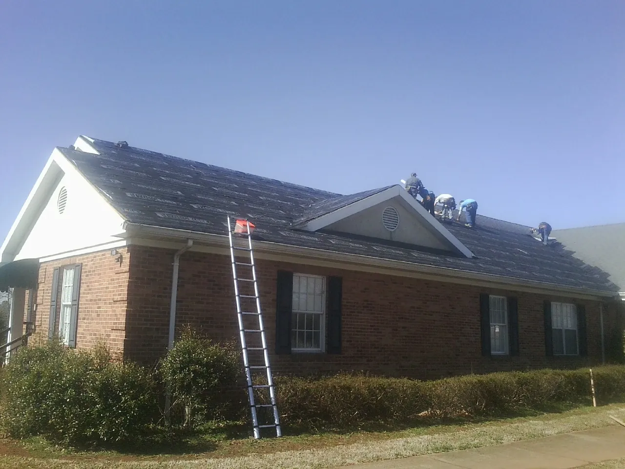 Crew tearing shingles off a brick ranch roof with a ladder set — Emergency Roof Repair work by our crew in Glenmont