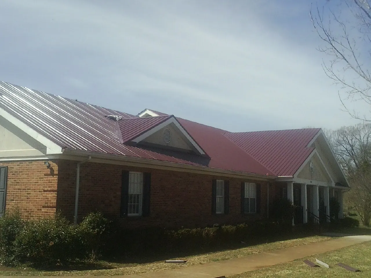Red metal roof with gabled entries on a long brick building, from a Hail Damage Roof Repair job in Glenmont