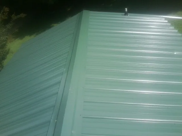 New green metal panels meeting at the ridge of a roof — Flat Roof Repair work by our crew in Glenmont