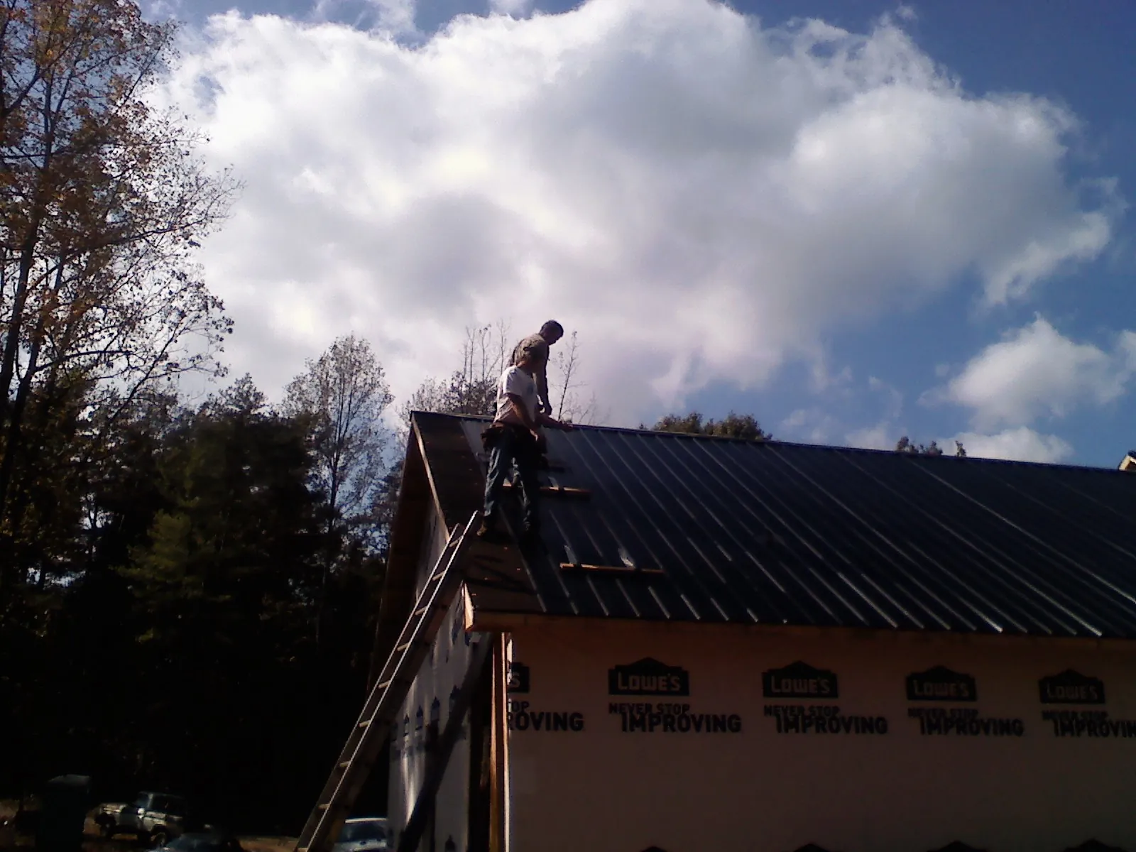 Roofer fastening dark metal panels high against a cloudy sky, from a Roof Inspection job in Glenmont