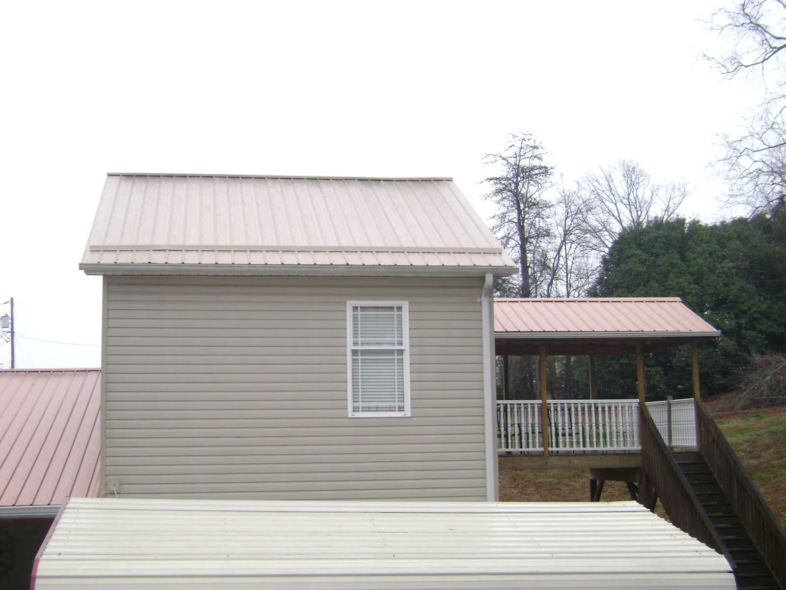Tan metal roofs on a two story addition and attached porch, from a Roof Replacement job in Glenmont